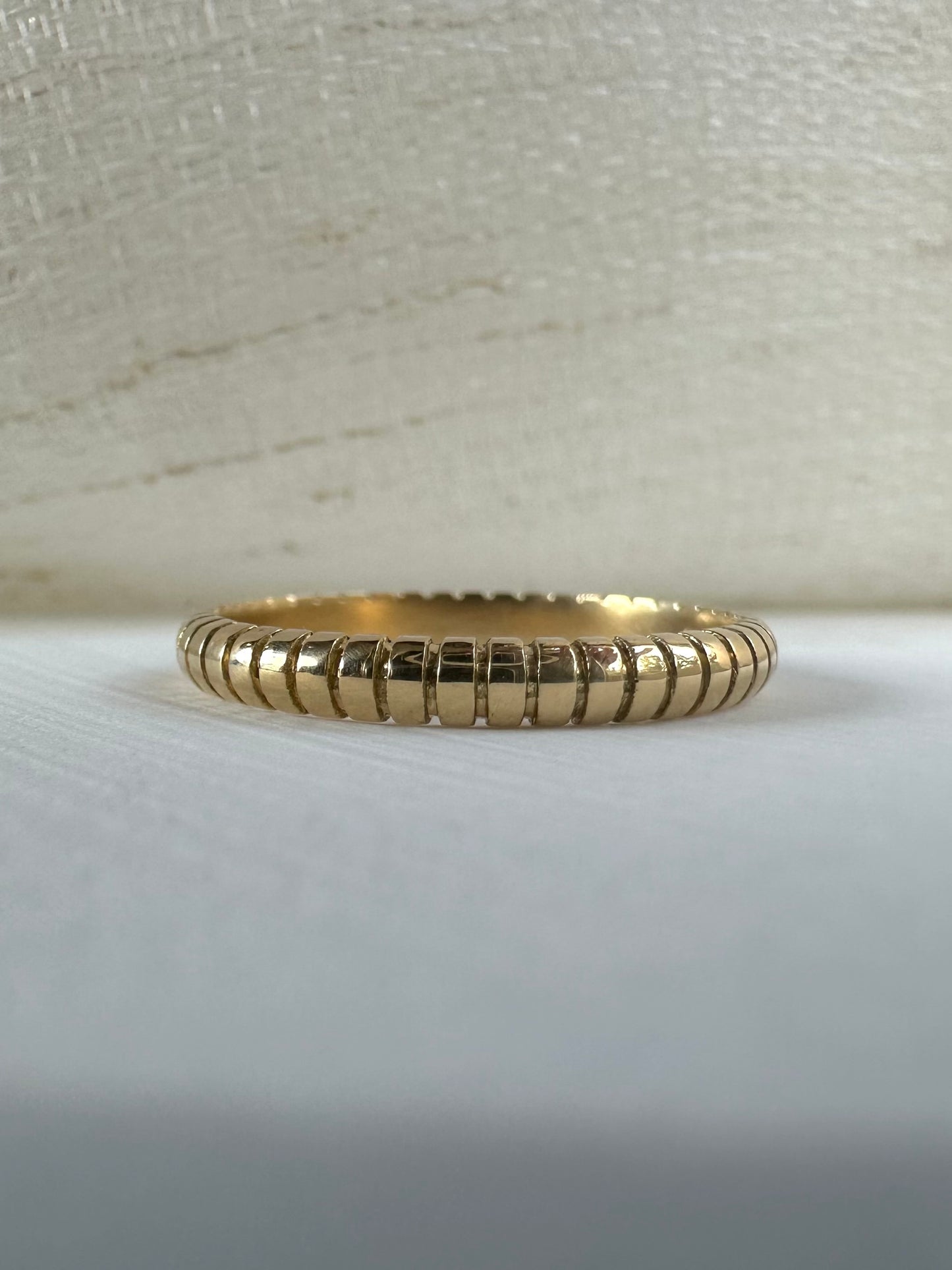 Thin 18k gold ribbed wedding band on finger
