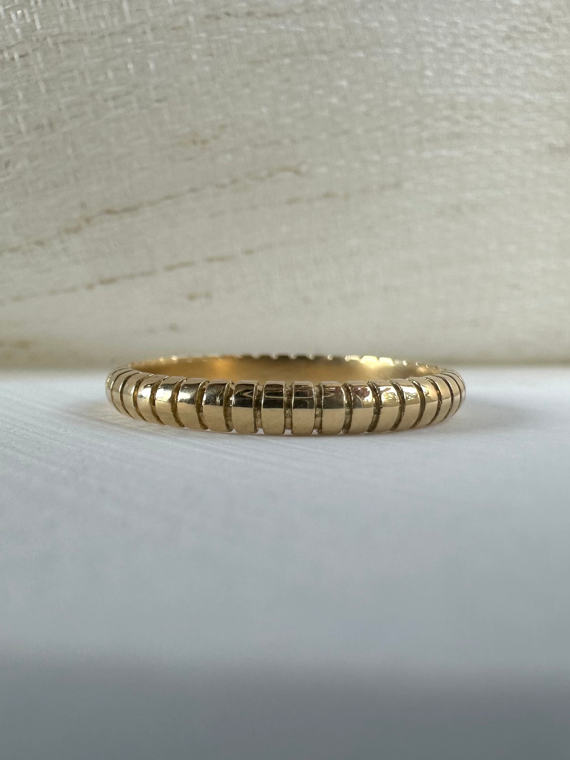 Thin 18k gold ribbed wedding band on finger