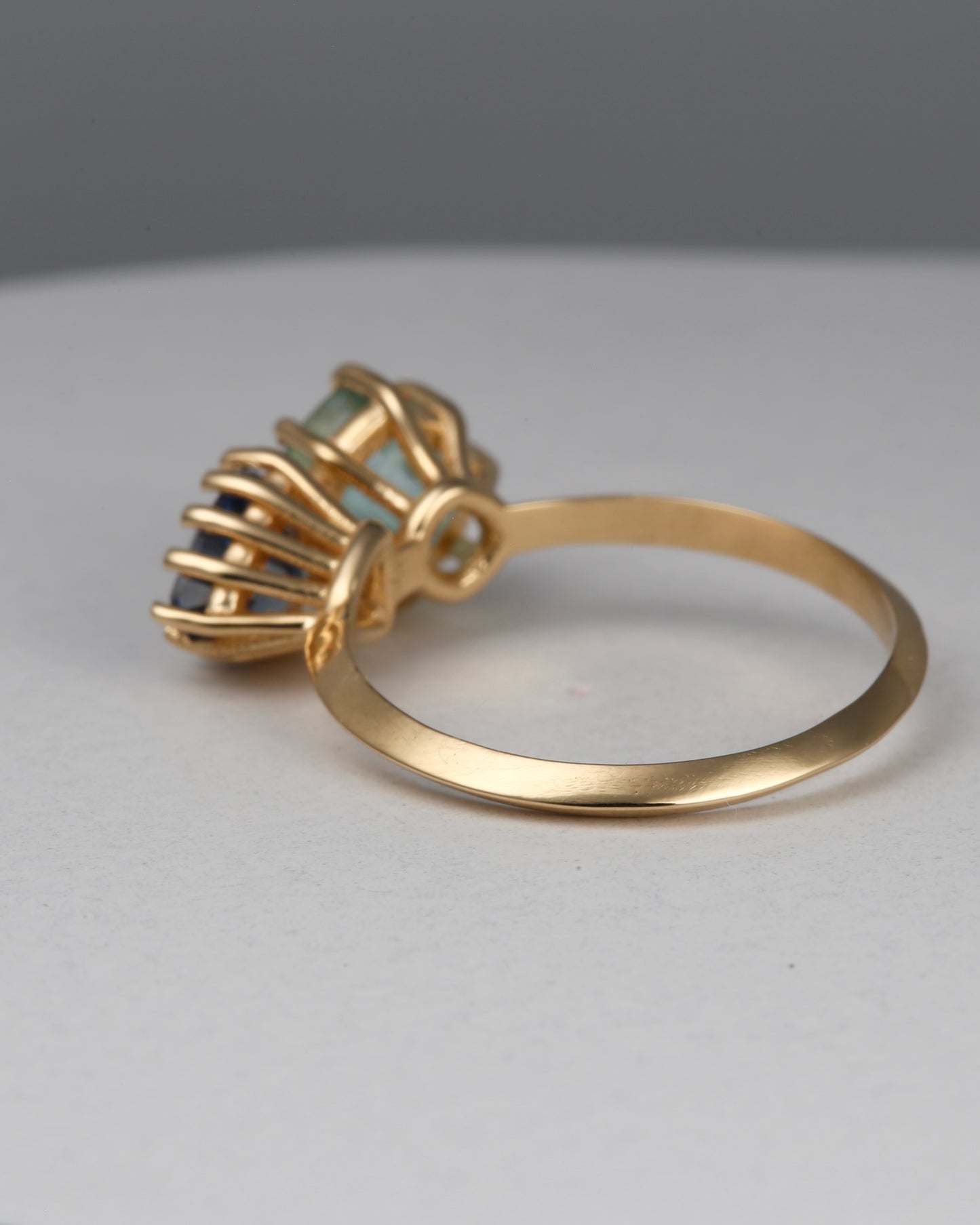 18K Toi et Moi ring features a cushion-cut green tourmaline paired with a triangular blue sapphire, creating a gorgeous and balanced contrast. Each stone is set in a distinct style: the green tourmaline in a claw prong setting, and the sapphire in a classic round prong setting.