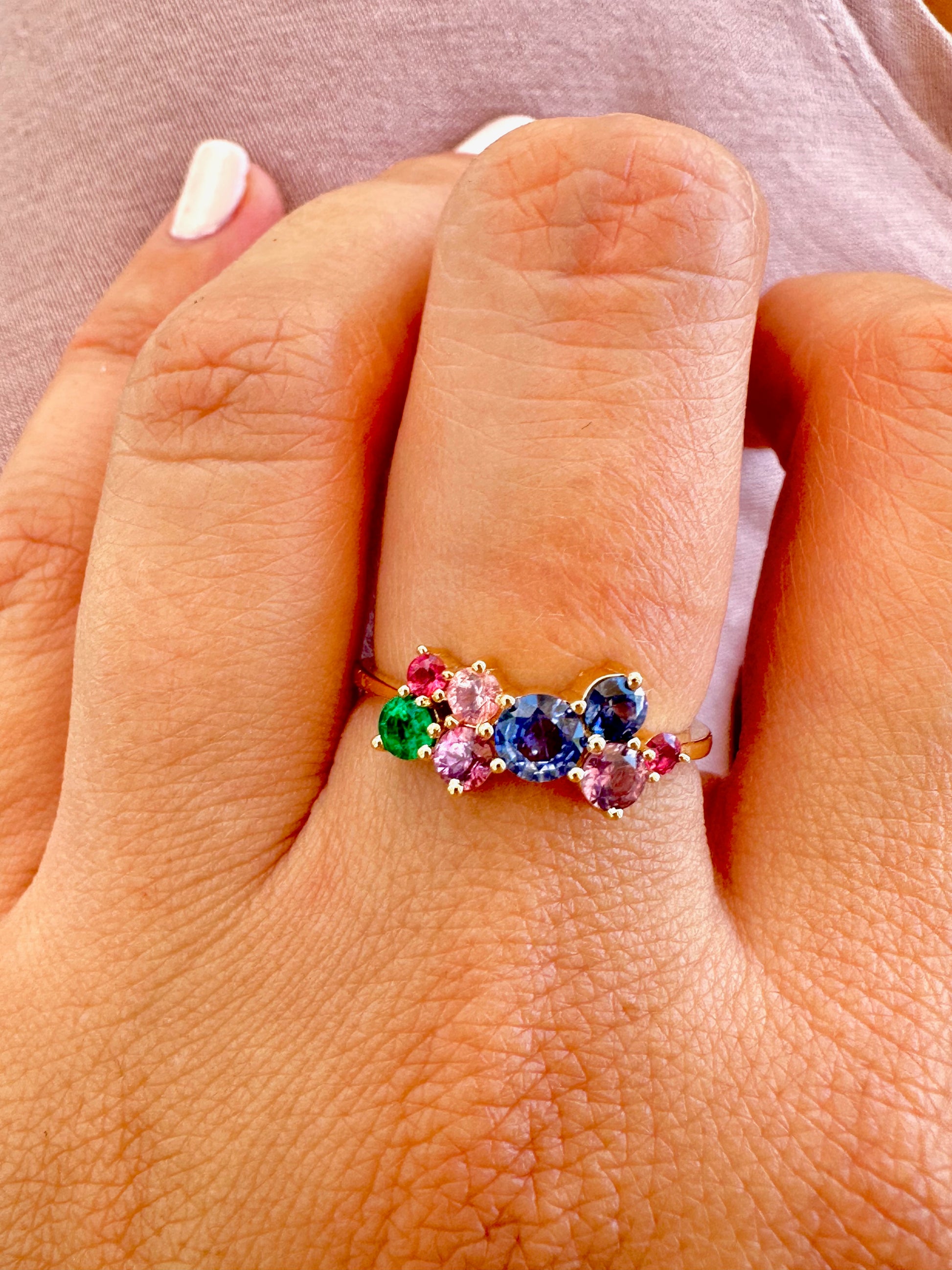 Rainbow Sapphire Ring features a stunning natural multicolor sapphires in a cluster ring design. The various Sapphires, of different sizes and colors, along with one natural emerald, are placed randomly to form this beautiful rainbow ring.
This ring is set in a timeless classic 18 karat gold, featuring a dainty band. | Ella Creations Jewelry 